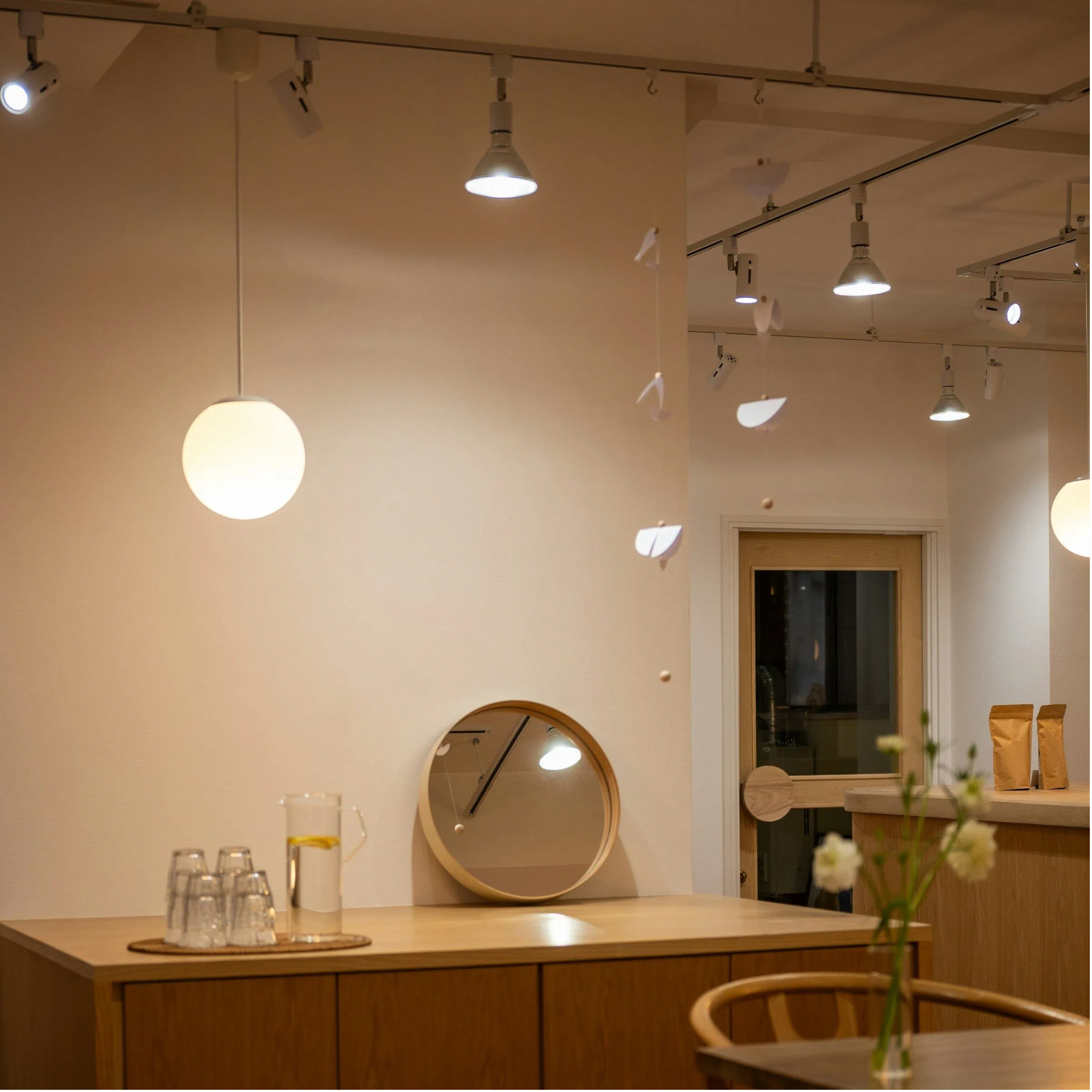 Modern cafe interior with white track lighting system featuring adjustable spotlights and globe pendant lights on ceiling mounted H-type rail for commercial kitchen and dining area