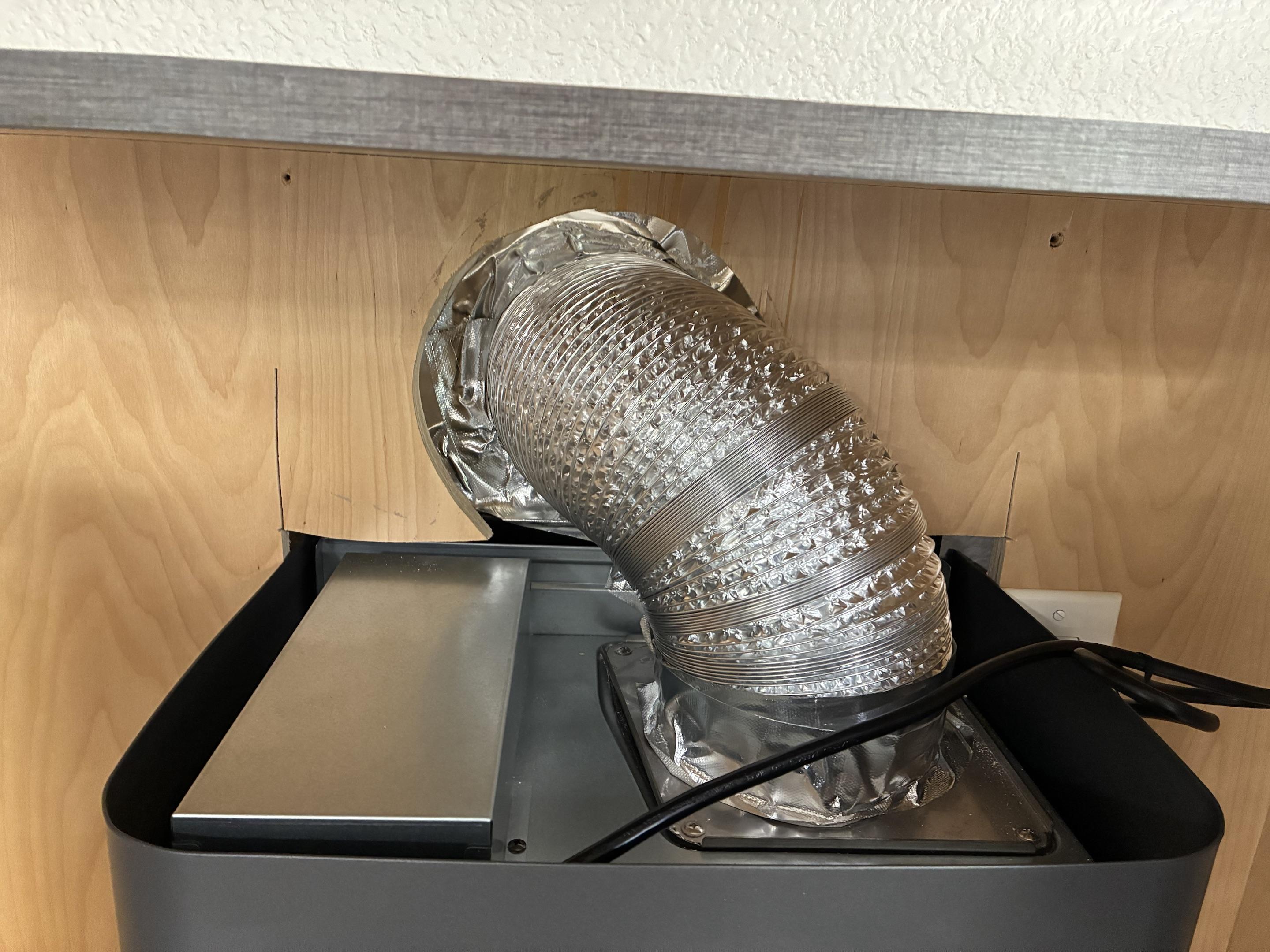 Incorrect flexible corrugated aluminum foil duct with visible ridges connected to range hood outlet inside cabinet demonstrating improper installation that reduces airflow