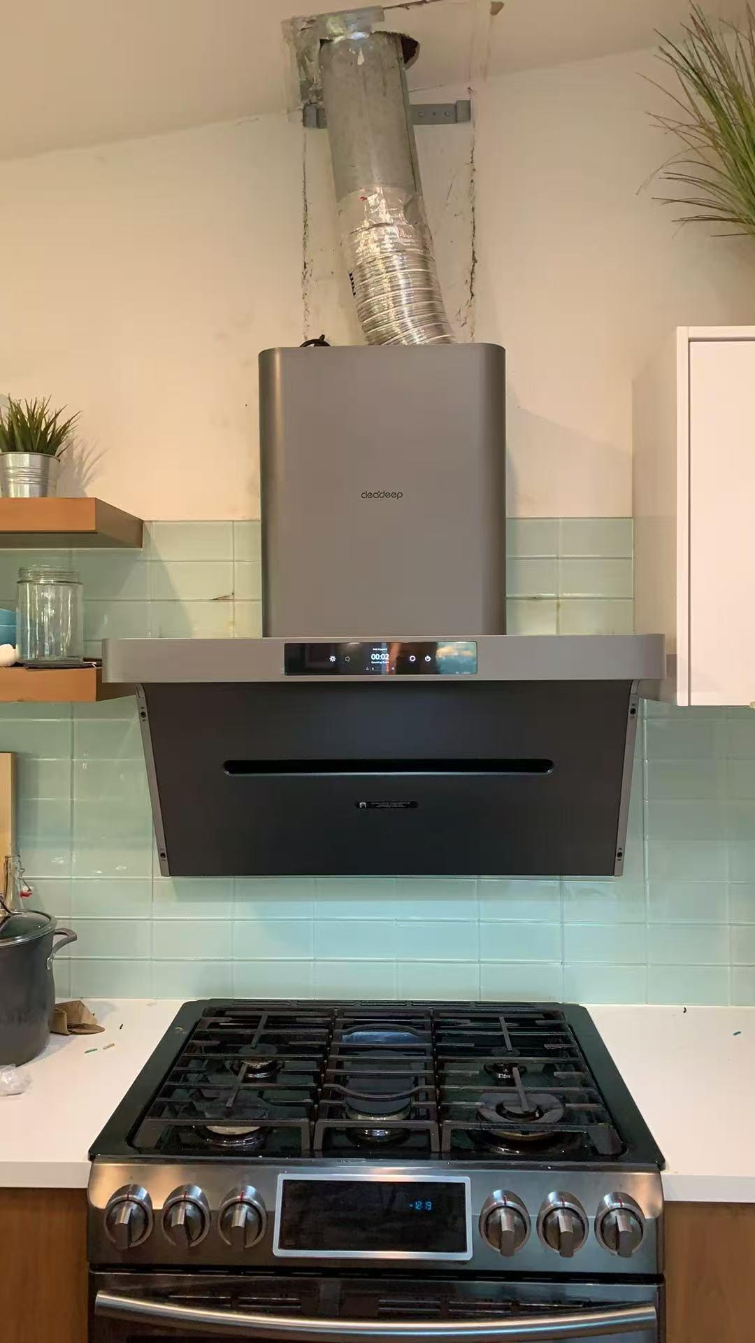 Black wall-mount chimney range hood with rigid metal ductwork extending through ceiling in modern kitchen with mint green subway tile and gas cooktop