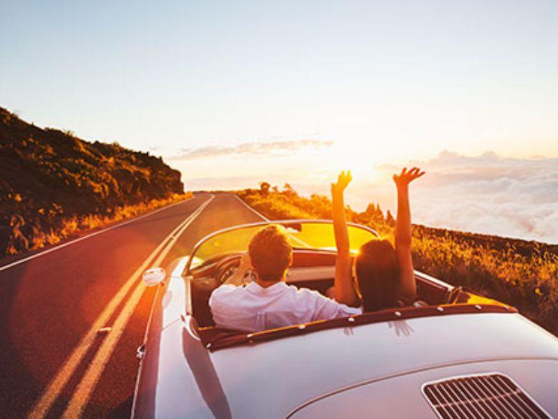 Couple driving convertible into sunset; travel blogging inspiration