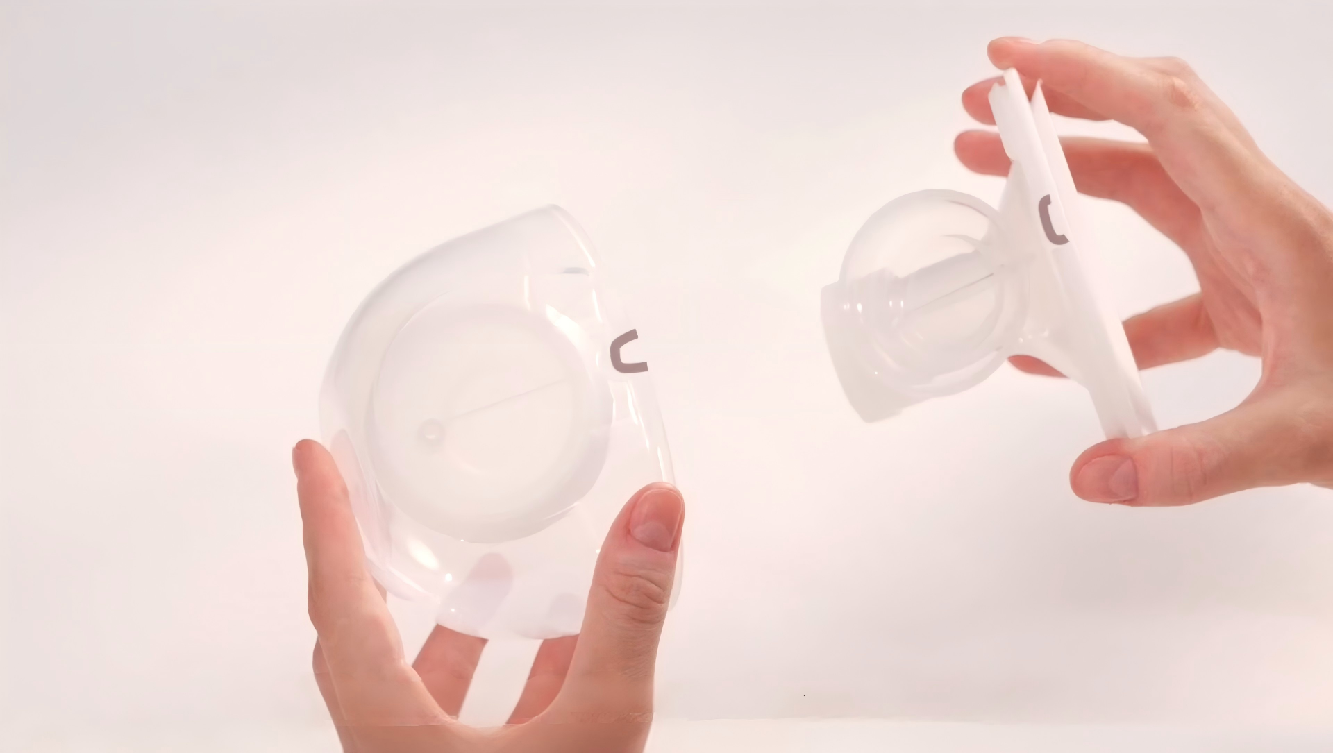 Hands hold two parts of clear plastic breast pump flange