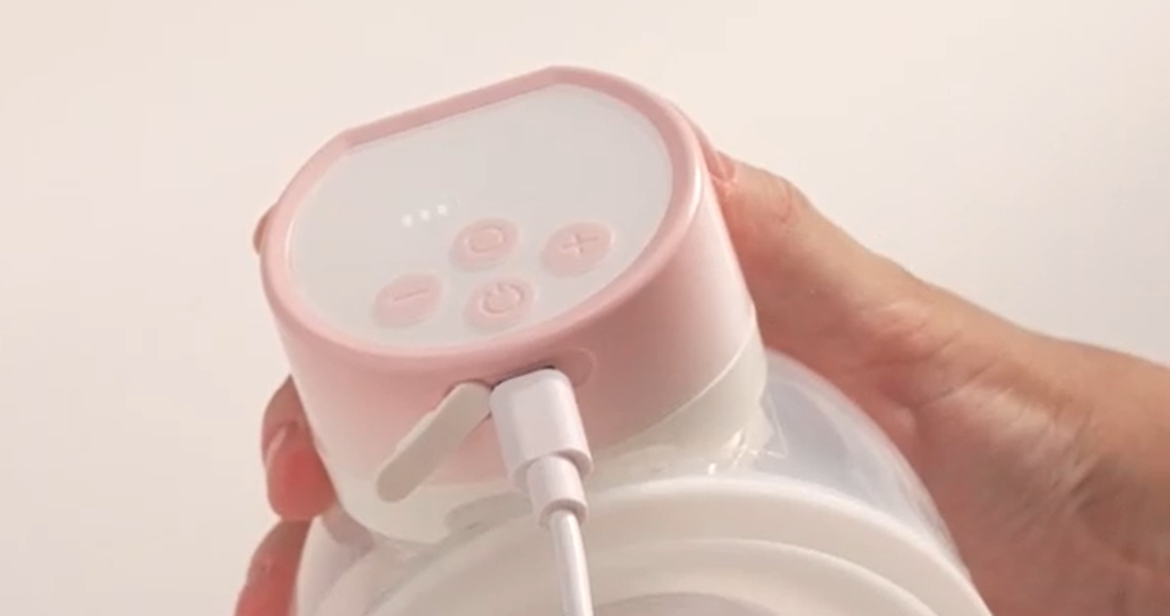 Pink portable breast pump being charged with USB cable